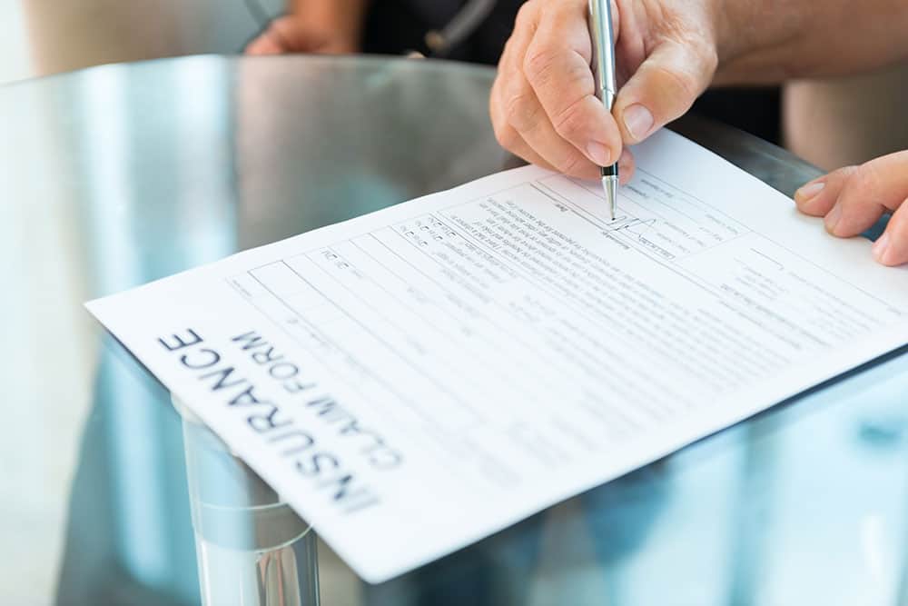 Closeup of a man's hand signing an insurance claim form